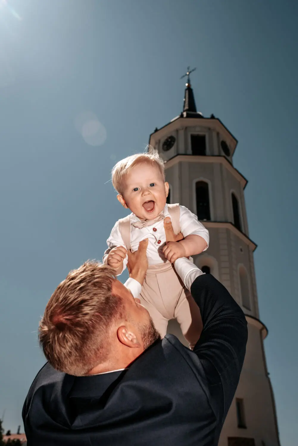 Tėvas iškelia savo berniuką aukštyn, saulėta vasaros diena, katedros varpinė fone