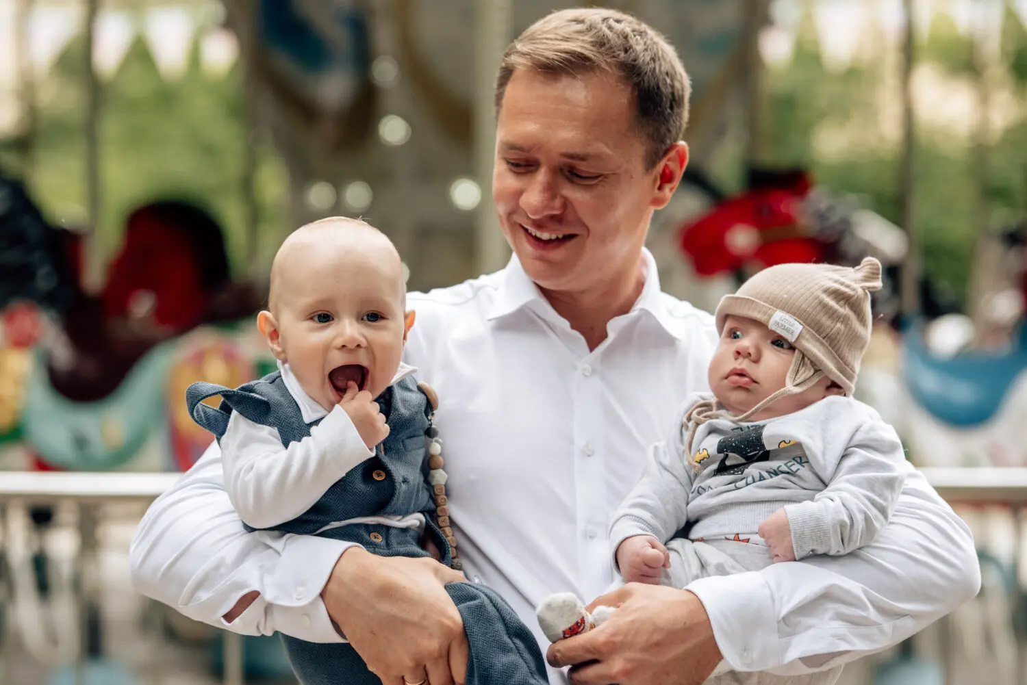 Tėvas ir du kūdikiai prie karusėlės sode