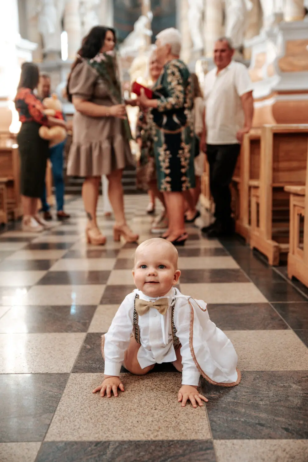 Berniukas šliaužioja bažnyčios grindimis, jo mama ir seneliai fone