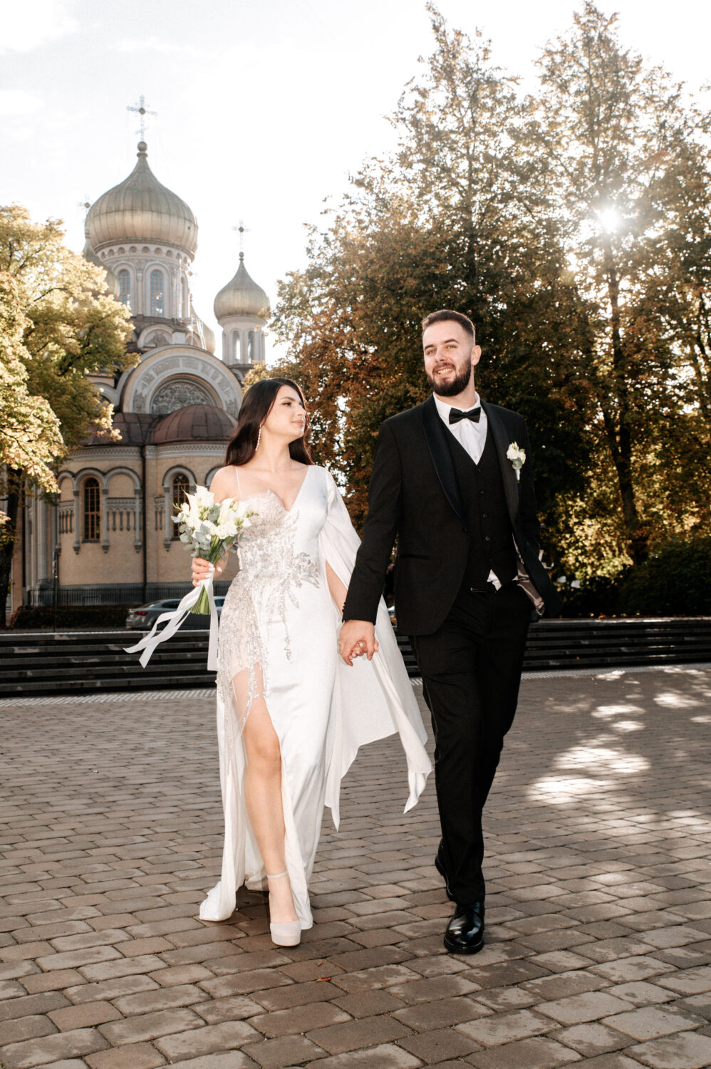 Jaunavedžiai eina susikabinę rankomis senamiesčio gatve ir žiūri viens į kitą