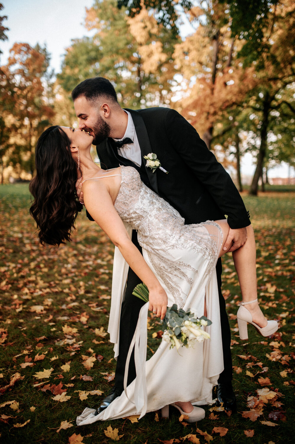 Jaunavedžiai pereina akmenimis grįstą gatvę, jaunikis atsisuka į jaunąją, jie šypsosi.